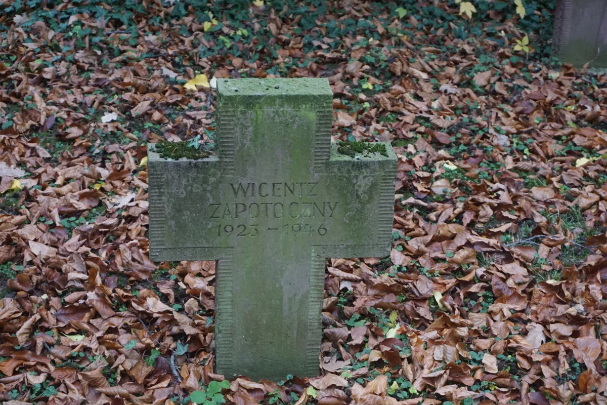 Kamienny krzyż porośnięty mchem, wśród liści.
Napis: „WICENTZ ZAPOTOCZNY 1923–1946”