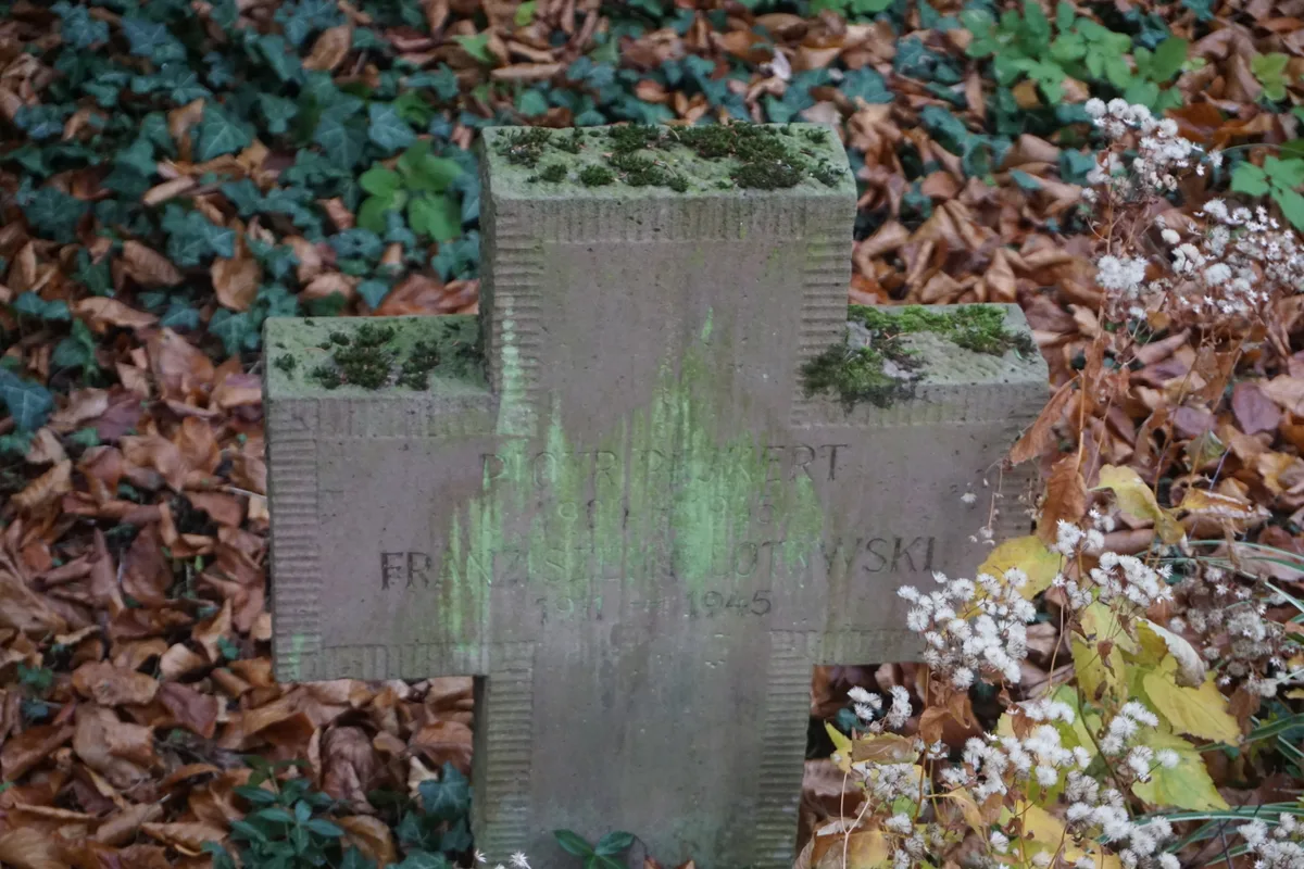 Kamienny krzyż z dwoma nazwiskami, mocno zabrudzony zielonym nalotem; napis częściowo nieczytelny.
Napis: „PIOTR PE?KERT 19?? – 19?? | FRANZIS??? ??OT??WSKI 1911 – 1945”