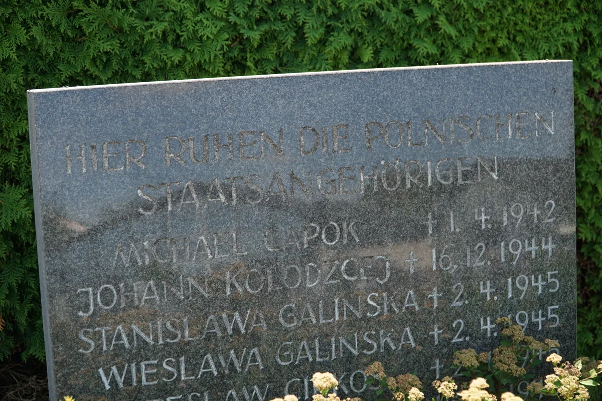 Zbliżenie górnej części płyty z nagłówkiem i pierwszymi nazwiskami.
Napis: „HIER RUHEN DIE POLNISCHEN STAATSANGEHÖRIGEN | MICHAEL CAPOK +1.4.1942 | JOHANN KOLODZCEJ +16.12.1944 | STANISLAWA GALINSKA +2.4.1945 | WIESLAWA GALINSKA +2.4.1945 | …SLAW CI?KOS”