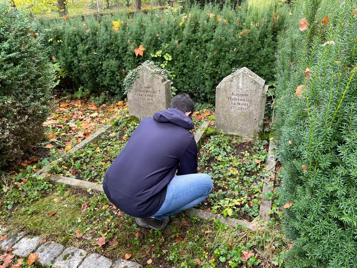 Dwa kamienne nagrobki z obramowaniem, mężczyzna (od tyłu) przy pracach porządkowych.
Napis: „Tadeus Jedrzejewski 23.4.1924 3.12.1947 | Kasimir Walerowicz *6.11.1911 †2.3.1945”